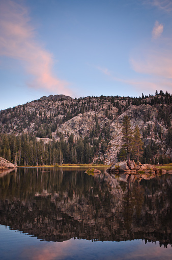 Landscape of the Sierra Nevada Mountains in California USA with a calm quiet lake below that reflects the sky at sunset.