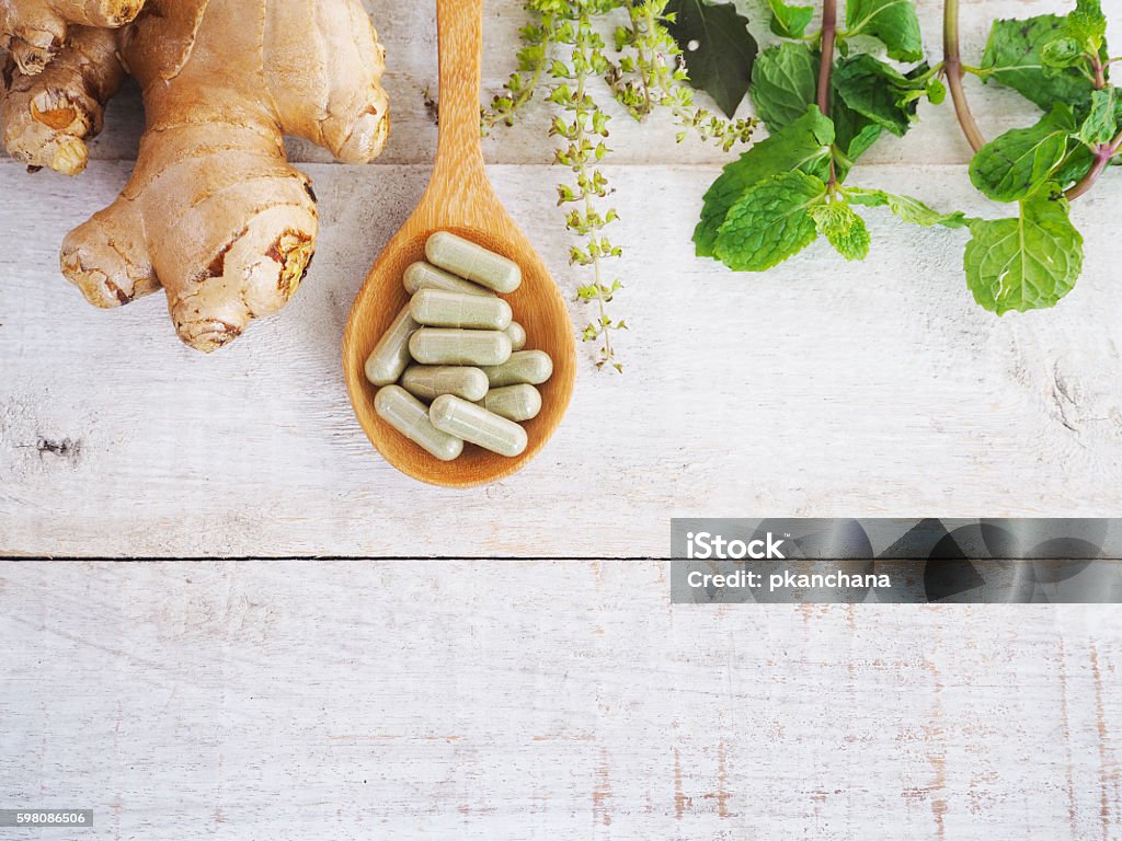 herbal pills on wooden spoon and green herb. herbal pills on wooden spoon with ginger root and green plant on wood background.Above view Nutritional Supplement Stock Photo