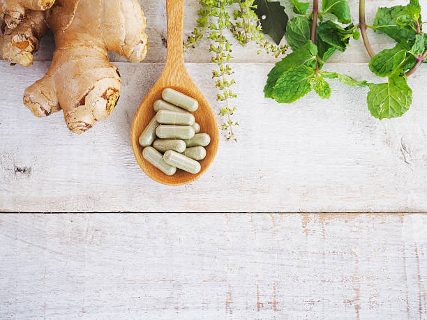 herbal pills on wooden spoon and green herb. herbal pills on wooden spoon with ginger root and green plant on wood background.Above view nutritional supplement photos stock pictures, royalty-free photos & images