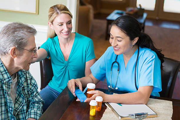 Hispanic nurse visits with senior patient in his home Pretty Hispanic mid adult nurse talks with a senior male patient and his daughter. The nurse is organizing the man's medicine in a pill organizer. Drug And Alcohol Treatment Programs For Your Loved One stock pictures, royalty-free photos & images