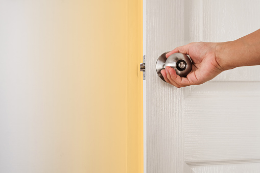 Hand holding door knob, white door and wall, with copy space