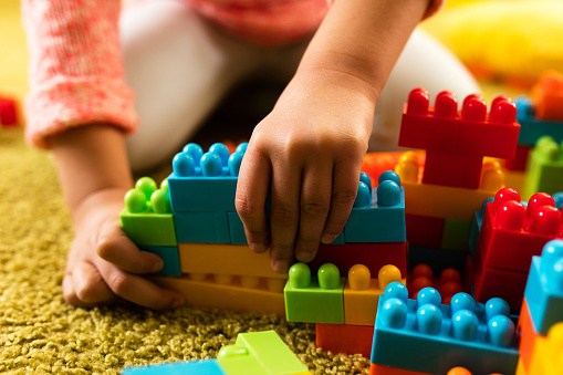 Close-up of  little girl building something with plastic blocks on the floor.