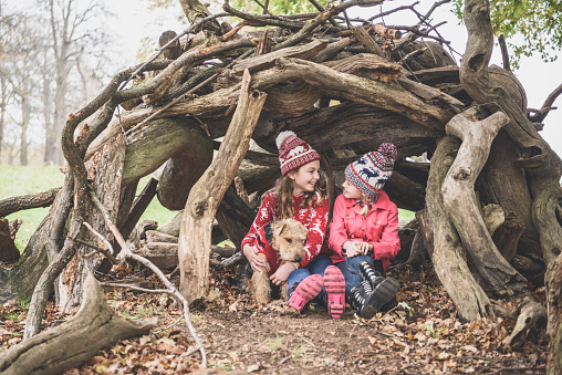 Two sisters in winter clothes in log den with dog
