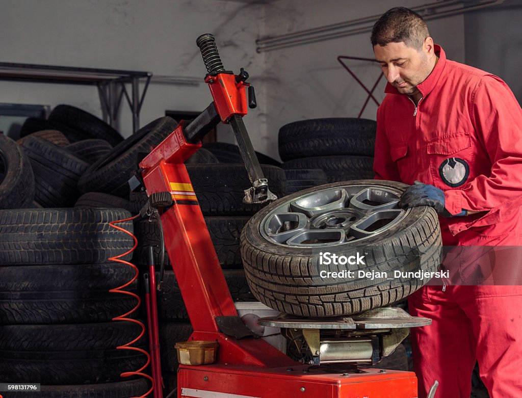 Mechanic replacing a tire on the wheel Mechanic replacing a flat tire from  wheel in his garage Adult Stock Photo
