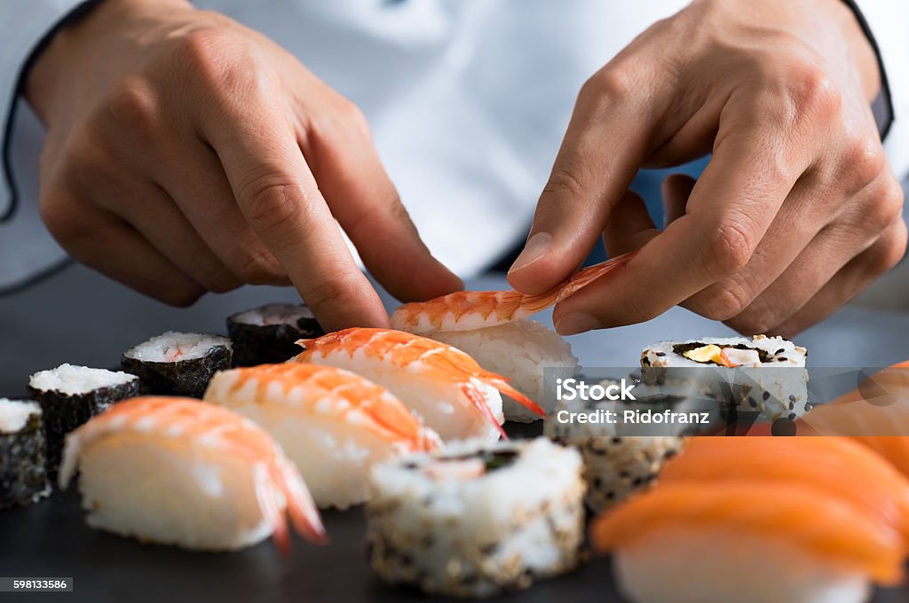 Chef preparing sushi Closeup of chef hands preparing japanese food. Japanese chef making sushi at restaurant. Young chef serving traditional japanese sushi served on a black stone plate. Sushi Stock Photo