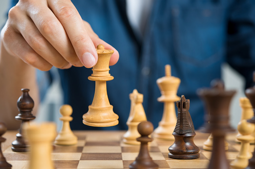 Close up of hand of man playing chess holding queen. Business man playing chess. Hand of casual businessman making a move with queen in chess. Business strategy and leadership concept.