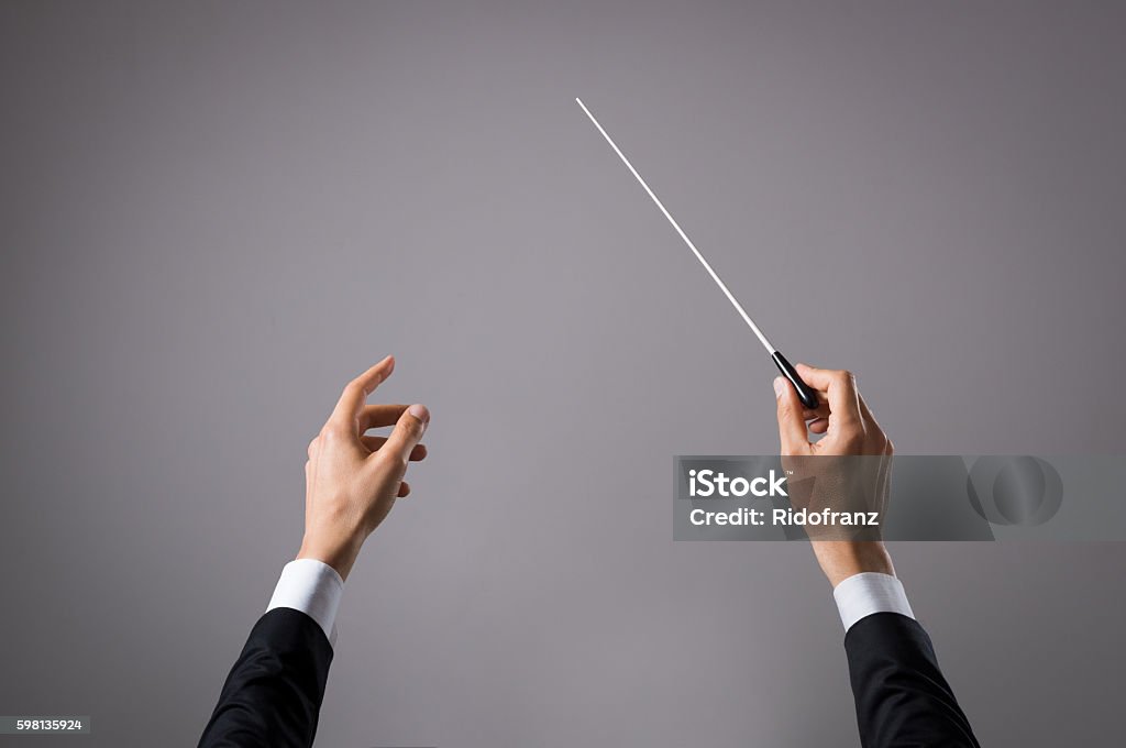 Musician directing concert Concert conductor hand with baton isolated on grey background. Chorus composer holding baton during a opera. Musician directing concert. Close up hands of orchestra conductor with copy space. Musical Conductor Stock Photo