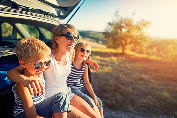Kids on a road trip in Tuscany, Italy Three kids resting on a road trip. Kids are aged 10 and 7 and are sitting in an opened car trunk. The kids are laughing and embracing, Sunny summer day in Tuscany, Italy. exhilaration photos stock pictures, royalty-free photos & images