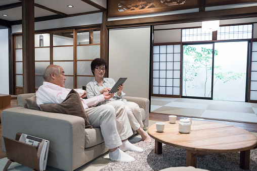 Senior man and mature woman on sofa in Japanese home with digital tablet