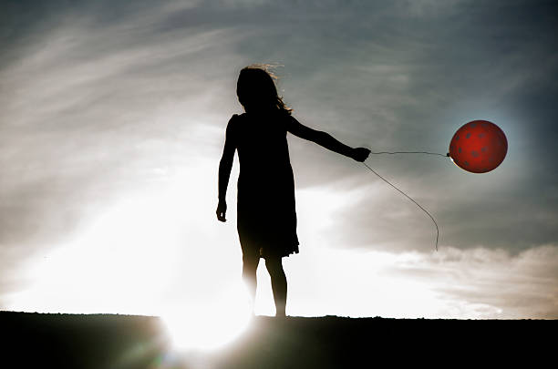 istock Girl holding a red dot balloon in sunset light 598147738