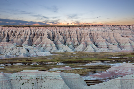 Scenic sunset view of the geological formations of the South Dakota badlands with heavily eroded buttes, gullies and spires rising from the surrounding prairie grassland