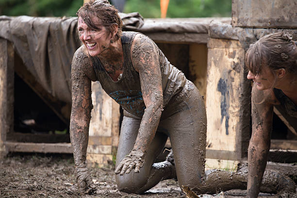 Laughing muddy woman emerging from a muddy tunnel Сirencester, England - August 21, 2016: Laughing muddy woman emerging from a 'Tough Mudder' tunnel obstacle during her gruelling 12 mile assault course challenge in Cirencester park, Gloucestershire. This annual event is a team-based 10-12 mile obstacle course designed to test physical strength endurance and teamwork. man laughing hard stock pictures, royalty-free photos & images