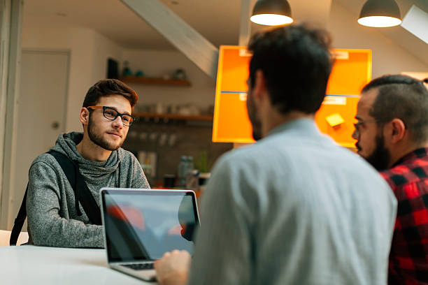 Young man at a job interview. Young man at a job interview talking with two developers. They are running startup developer company from their home. Side view of them discussing. casual job interview stock pictures, royalty-free photos & images