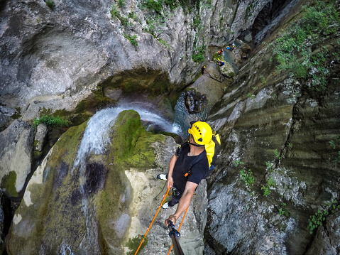 Canyoneering member with selfie stick rappeling down the waterfall in the canyon.