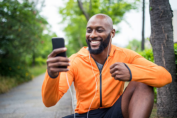 Happy with the results African american man sitting outdoors before his training. He is holding mobile phone and looking at it. black orange audio stock pictures, royalty-free photos & images