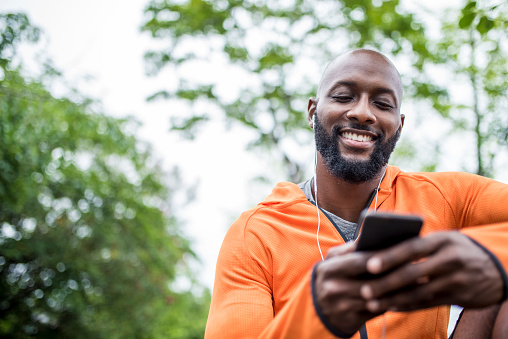 African american man sitting outdoors before his training. He is holding mobile phone and looking at it.