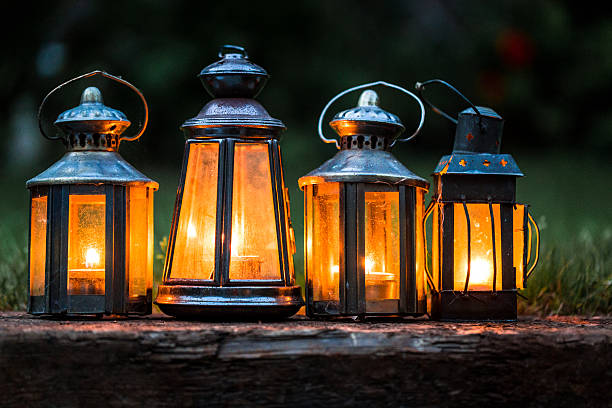 Four differrent antique lanterns in a row. The lanterns are illuminated by candles inside, giving off a warm orange glow. Horizontal close up colour image with copy space.