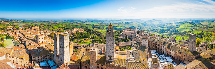 Panoramic aerial vista across the rooftops and iconic stone towers of San Gimignano, the medieval hilltop town set amongst green vineyards in the heart of Tuscany, Italy.