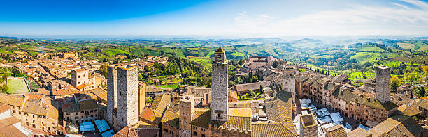 Italy San Gimignano medieval towers terracotta rooftops iconic town Tuscany Panoramic aerial vista across the rooftops and iconic stone towers of San Gimignano, the medieval hilltop town set amongst green vineyards in the heart of Tuscany, Italy. siena italy stock pictures, royalty-free photos & images