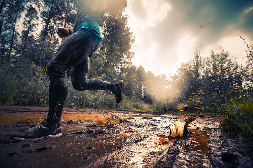 Trail running athlete crossing the dirty puddle in the forest