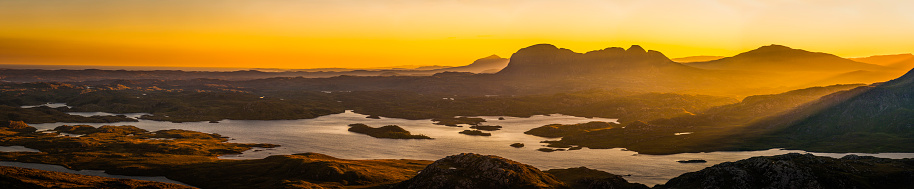 Golden rays of sunlight streaming through the glen to illuminate the remote mountain wilderness, lochs and landscapes of Sutherland in the north west highlands of Scotland, UK in this glorious daybreak panorama.