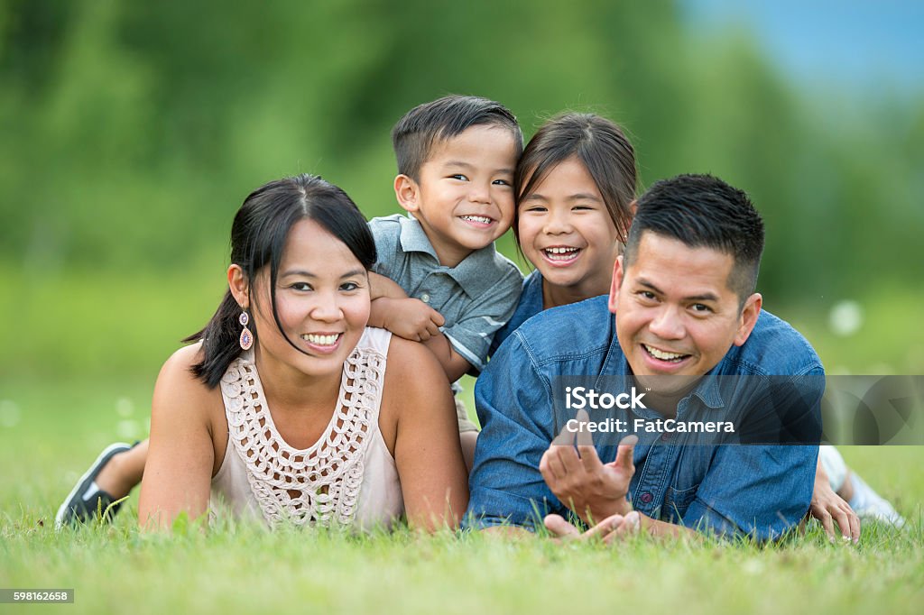 Family Portrait at the Park A family of four are lying together in the grass at the park and are smiling while looking at the camera. Asian and Indian Ethnicities Stock Photo