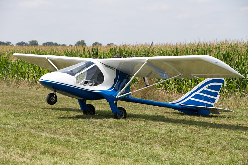 Small little single engine microlight experimental plane sitting in a field balance on its tail with the nose wheel in the air waiting for the pilot to return to counter the weight