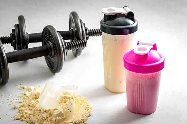 Fitness and workout concept Fitness and workout concept with dumbbells, protein shakers  and a scoop in protein powder. The two shakers have black and pink lids and the background is white protein stock pictures, royalty-free photos & images