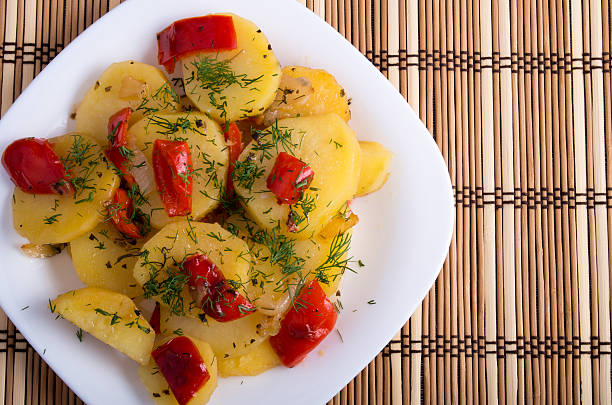 Top view of a vegetarian dish with organic vegetables - potatoes and stewed slices of red pepper on a wooden background