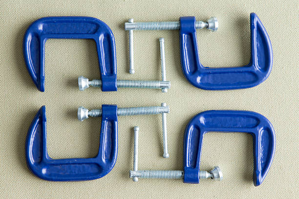 Four blue steel g-clamps neatly arranged on a beige background viewed from above in a DIY, renovation, repair and construction concept