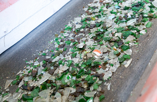Glass particles for recycling in a machine in a recycling facility. Different glass packaging bottle waste. Glass waste management. Glass recycling is the process of waste glass into usable products.