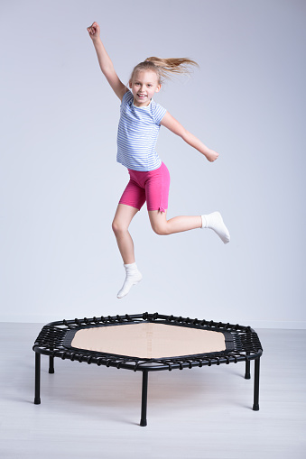 Happy school girl jumping on a small trampoline in a very bright room