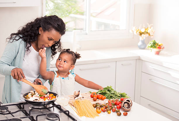 Mother and daughter cooking together. Mother with her 2.5 years little girl daughter preparing pasta with red sauce together. Woman and girl using fresh tomato, mushrooms, basil and garlic. ethiopian ethnicity photos stock pictures, royalty-free photos & images