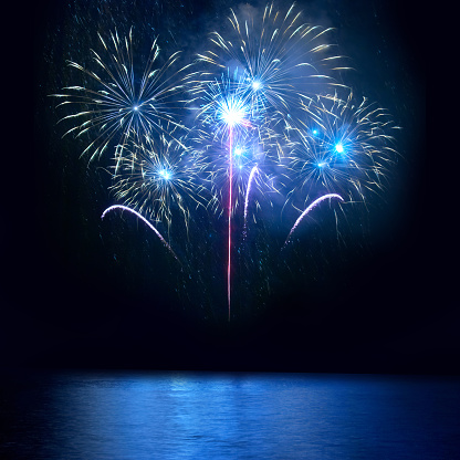 Blue fireworks above lake with reflection on water with black sky background