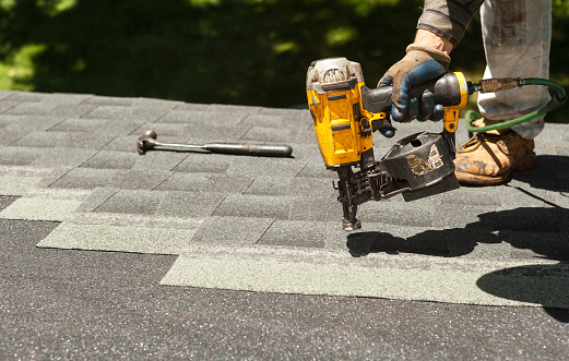 Roofers replacing old roof shingles with New shingles on residential home using a nail gun.