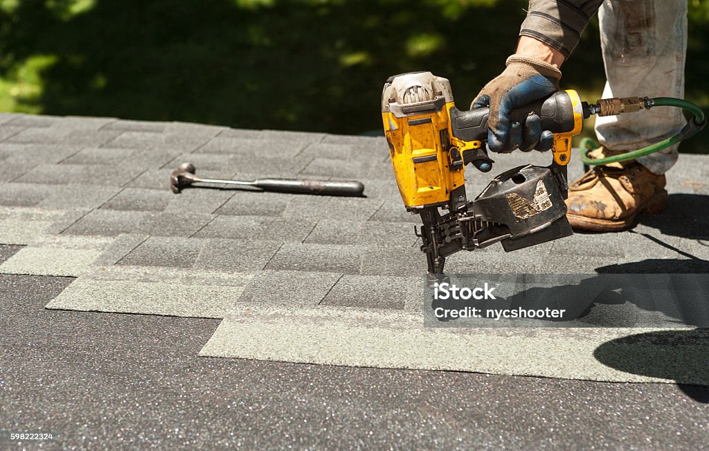 Roof shingle replacement Roofers replacing old roof shingles with New shingles on residential home using a nail gun. Rooftop Stock Photo