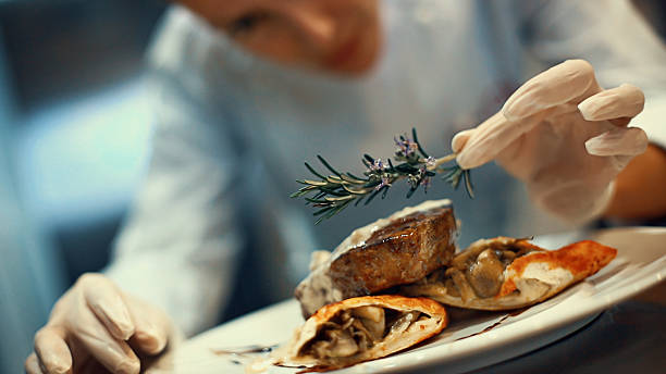 Chef placing finishing touches on a meal. Closeup tilt of blurry female chef placing rosemary on a steak meal before serving. She's using protective gloves when dealing with ready to eat food. dinner party photos stock pictures, royalty-free photos & images