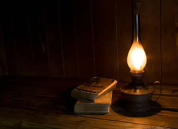 Old antique books with burning paraffin lamp near on the wooden table.