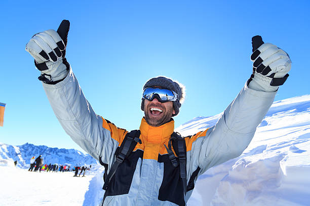 Male backpacker with thumbs up on top snow mountain Cheerful young man hiking on snow mountain. With ski wear, goggles, gloves and knit hat, backpack. Smiling with thumbs up. On background tourists and snow mountain peak. thumbs up for skiing stock pictures, royalty-free photos & images