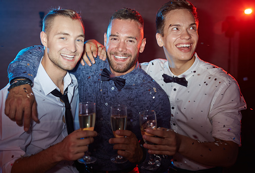 Three elegant guys holding flutes with champagne