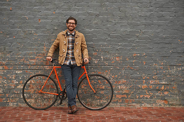 My daily commute is a green one Portrait of a young man posing with his bicycle against a grey wall in the city hipster bike stock pictures, royalty-free photos & images