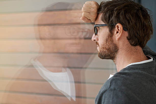 What could you achieve if you feared nothing? Shot of a thoughtful young entrepreneur leaning against a glass window in his office grim stock pictures, royalty-free photos & images