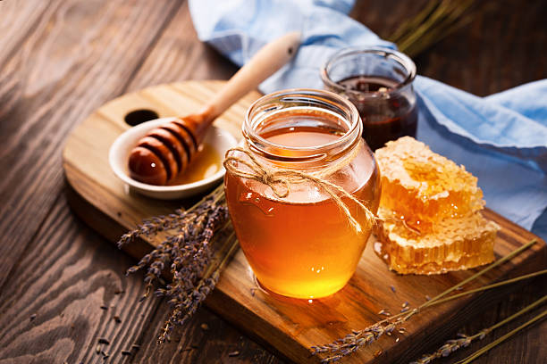 Honey in jar and bunch of dry lavender Jar of liquid honey with honeycomb inside and bunch of dry lavender over old wooden table. Dark rustic style, selective focus honeycomb animal creation photos stock pictures, royalty-free photos & images