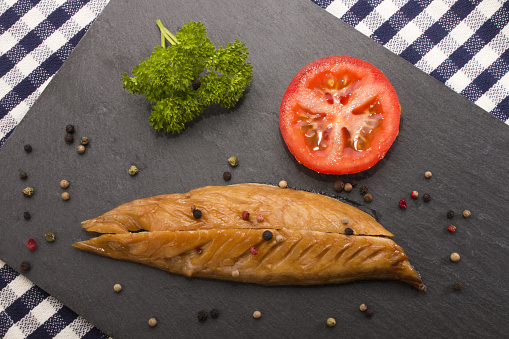 smoked mackerel with a slice tomato, parsley and mixed peppercorn on a slate plate