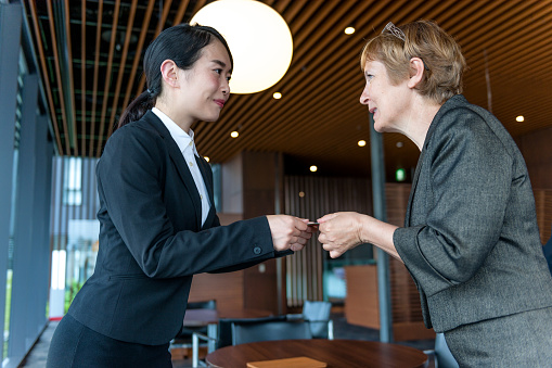 Mature Caucasian businesswoman and a young Japanese businesswoman/Business women exchanged business cards, Kyoto, Japan, Asia. Women in charge. Office interior, copy space. Nikon D3x, full frame, XXXL. iStocklypse Kyoto 2016.