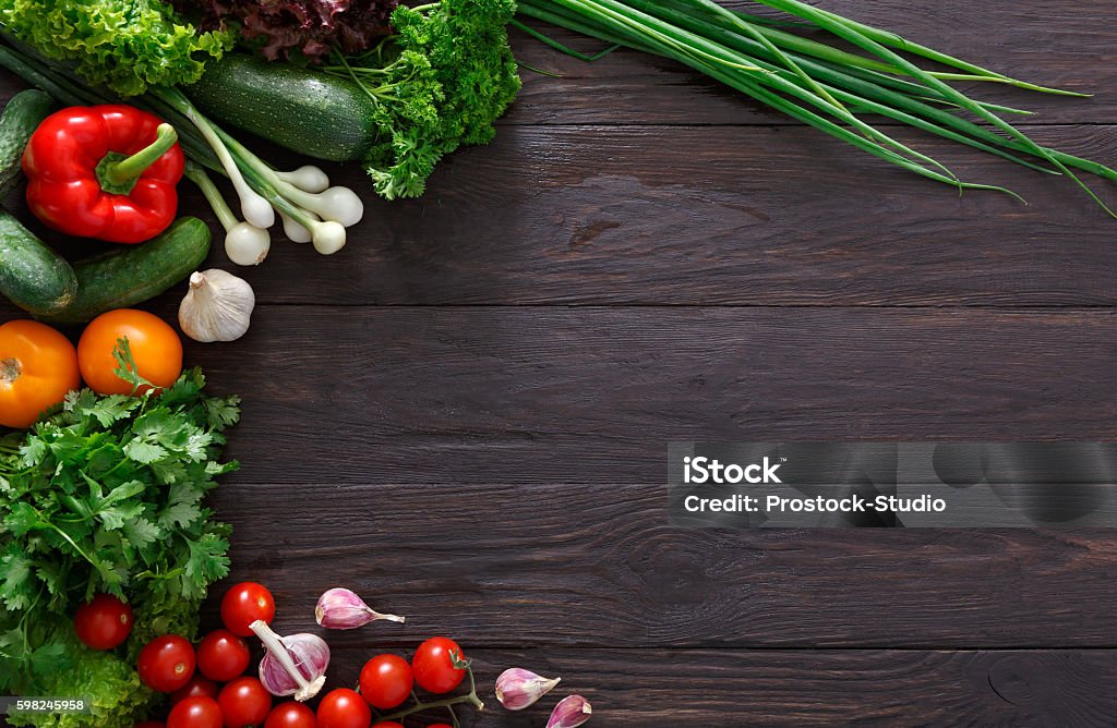 Border of fresh vegetables on wooden background with copy space Border of fresh organic vegetables on wood background. Healthy natural food on rustic wooden table with copy space. Garlic, lettuce, carrot, pepper, zucchini and other cooking ingredients top view Vegetable Stock Photo