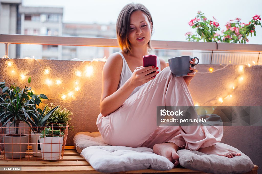 Special moment on terrace Women enjoy her special moment on terrace. She using her smartphone and sitting on pallet. Balcony Stock Photo