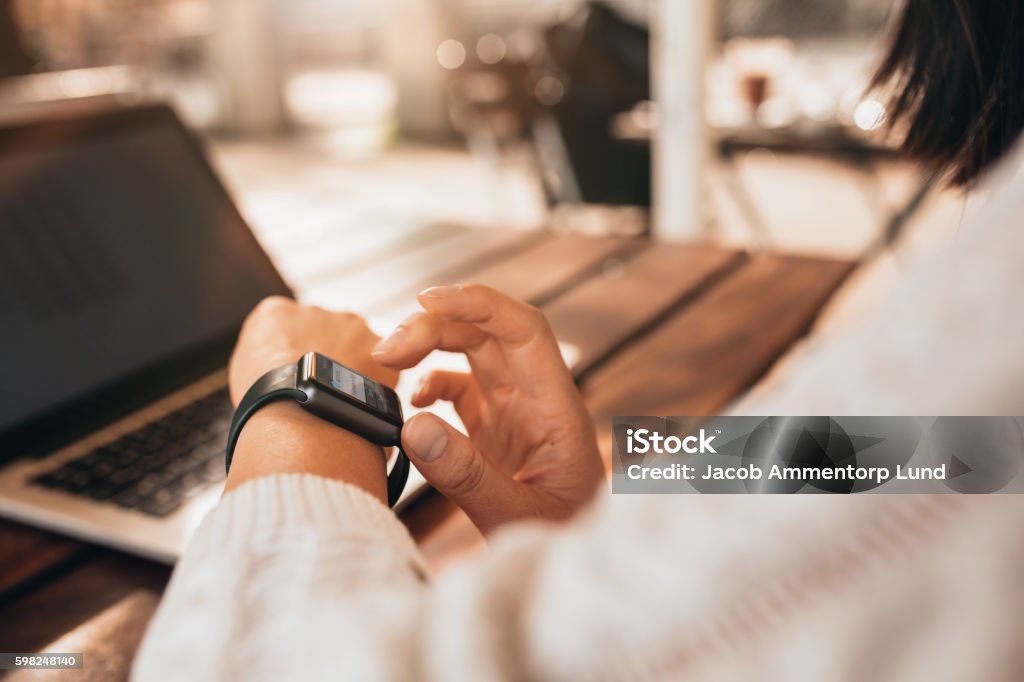Young woman using smartwatch at a cafe Close up of young woman using smartwatch at a cafe. Female sitting at a table and checking her smart watch. Smart Watch Stock Photo