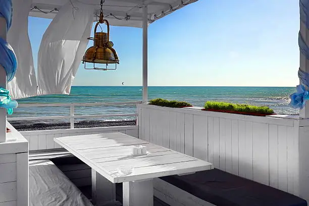 Seaview Restaurant Interior. White Terrace Or Veranda With Separated Cabins Under Tent And White Curtains. Wooden Furniture.  Hanging Lanterns.