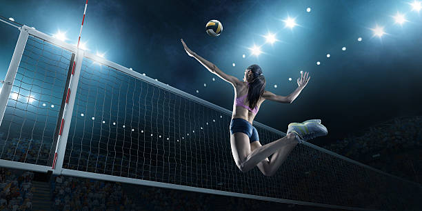 Volleyball: Female player in action Beautiful female volleyball player performs an emotional game moment on the indoor volleyball stadium with bleachers full of people. She is wearing an unbranded sports cloth. volleyball stock pictures, royalty-free photos & images